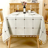 Refreshing sage green and beige windowpane plaid linen look tablecloth with white tassels on a rustic table