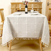 Modern grey windowpane plaid linen look tablecloth with white fringe tassels on a rustic wooden table