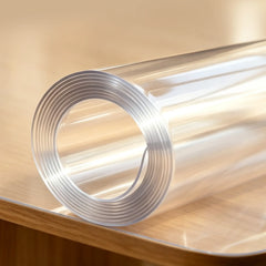 A rolled clear PVC table pad on a desk, showing material thickness and high-quality transparency.