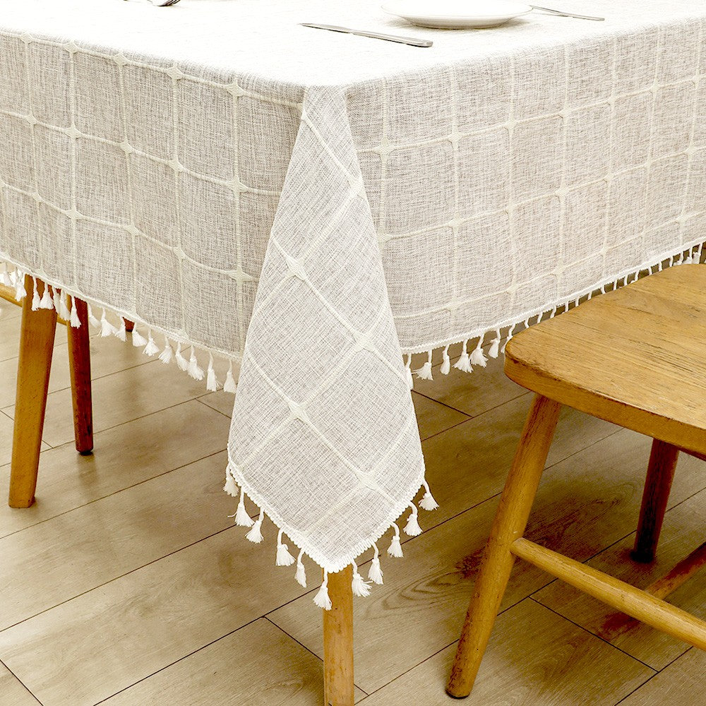 Close-up of intricate white macrame tassels on a grey grid lattice faux linen tablecloth