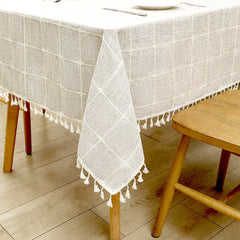 Close-up of intricate white macrame tassels on a grey grid lattice faux linen tablecloth