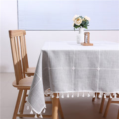 Cozy neutral dining room table styled with a grey plaid farmhouse tablecloth featuring white tassels and flower vase