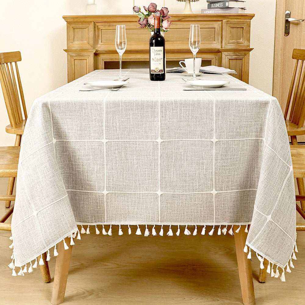 Modern grey windowpane plaid linen look tablecloth with white fringe tassels on a rustic wooden table