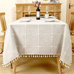 Modern grey windowpane plaid linen look tablecloth with white fringe tassels on a rustic wooden table