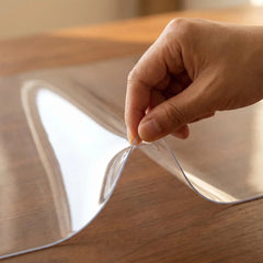 Lifting the edge of a clear PVC living room mat to show 1.5mm thickness, high transparency, and flexible texture.