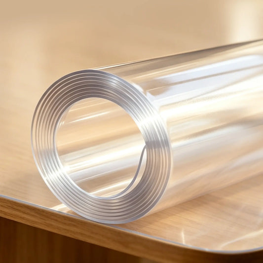 A rolled clear PVC table pad on a desk, showing material thickness and high-quality transparency.