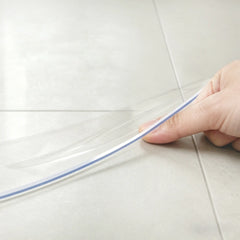 Hand pinching the edge of a round PVC mat to demonstrate 1.5mm thickness and crystal clear, premium quality.