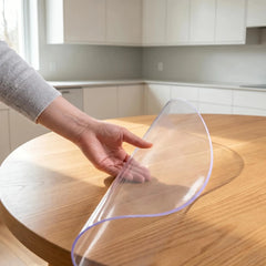 Hand pinching a round transparent PVC dining mat to show 1.5mm thickness and durable, flexible texture.