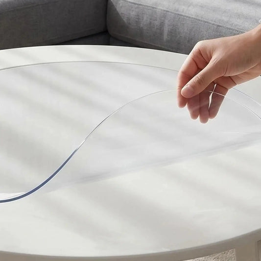 Hand pinching a round transparent PVC mat to show 1.5mm thickness and flexible, soft texture for furniture protection.