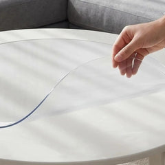 Hand pinching a round transparent PVC mat to show 1.5mm thickness and flexible, soft texture for furniture protection.